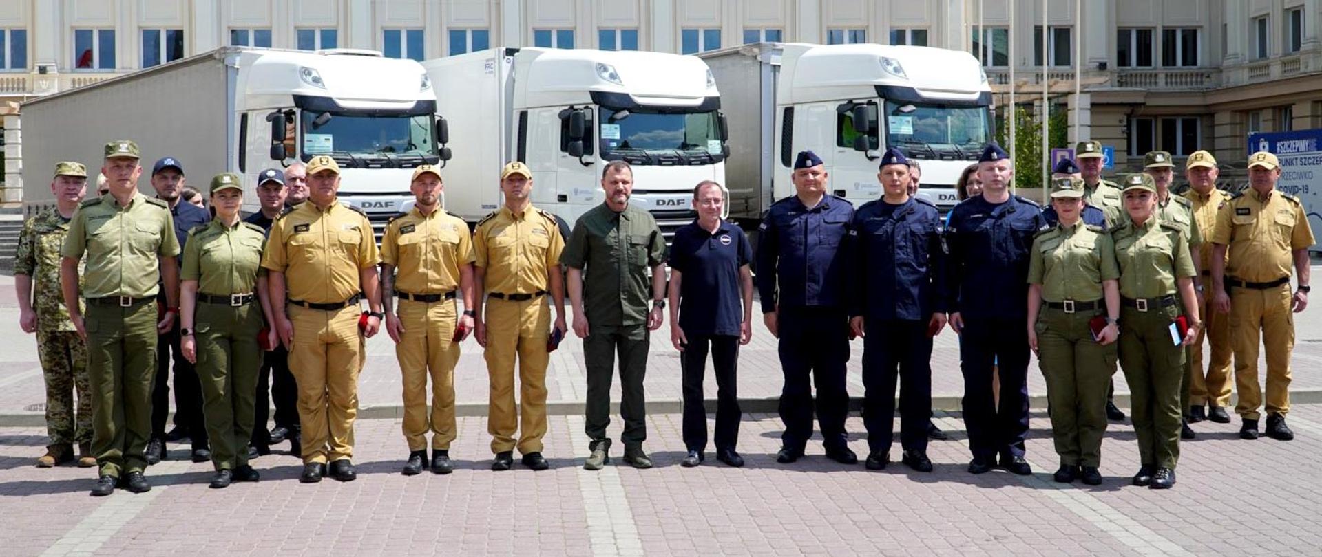 Zdjęcie zrobione przed Podkarpackim Urzędem Wojewódzkim w Rzeszowie podczas uroczystego wręczenia odznaczeń. Na placu stoją uczestnicy zbiórki. Wśród nich funkcjonariusze Państwowej Straży Pożarnej, Policji i Straży Granicznej.