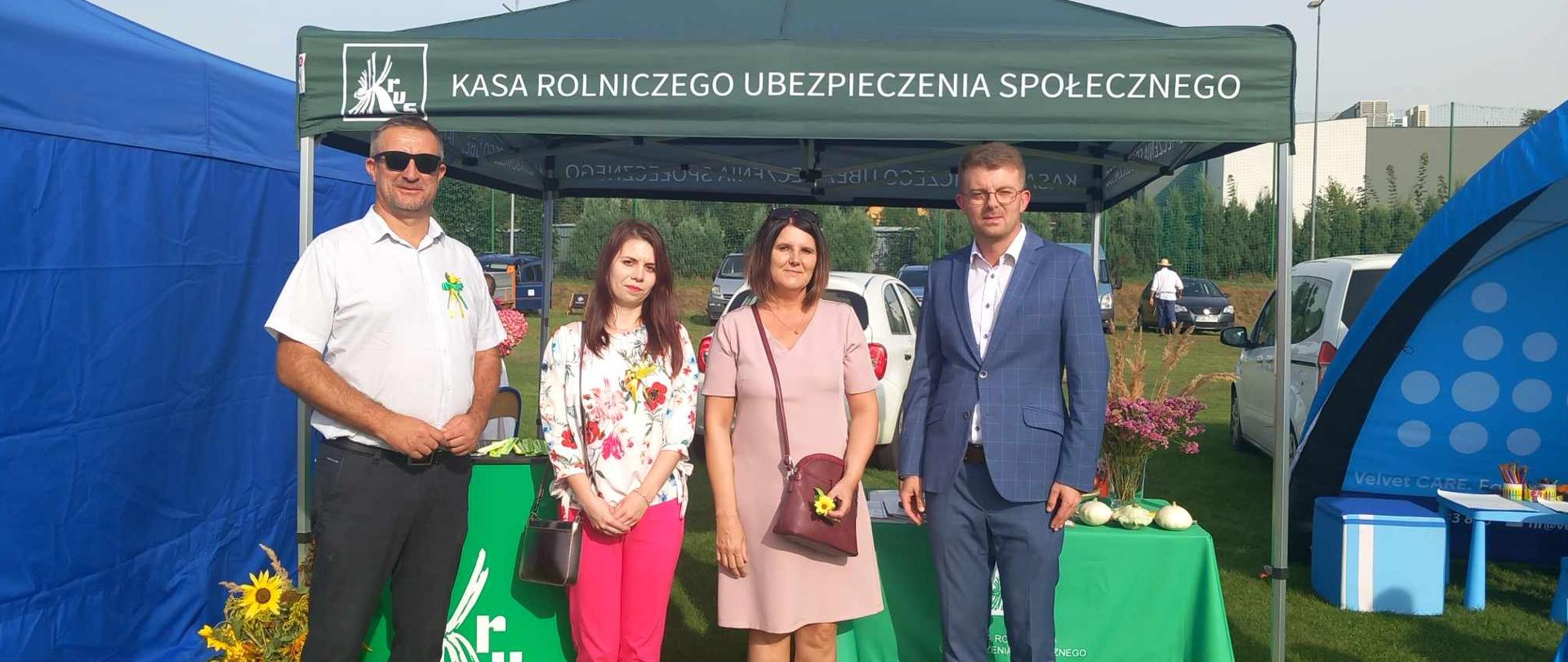 Na tle stoiska informacyjnego KRUS stoją dwie kobiety oraz dwóch mężczyzn. 