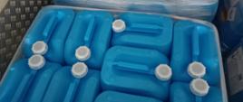Kilkadziesiąt błękitnych plastikowych kanistrów do przewozu cieczy. Pojemniki owinięte zbiorczo folią i znajdujące się w przestrzeni ładunkowej naczepy. Na bokach tych pojemników widoczne nalepki ostrzegawcze oznaczające m.in. materiał palny oraz zagrażający środowisku.