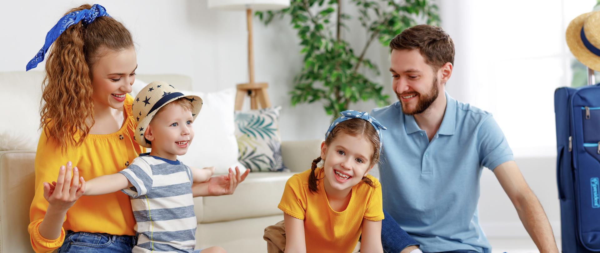 Happy parents with children laughing while sitting on floor near sofa with suitcases near at home