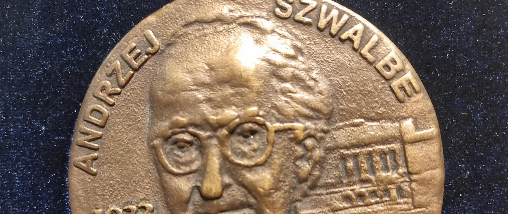 na zdjęciu okrągły medal w kolorze brązowym z wizerunkiem Andrzeja Szwalbego w środku na około napis Andrzej Szwalbe po lewej stronie data rok 1923-2002