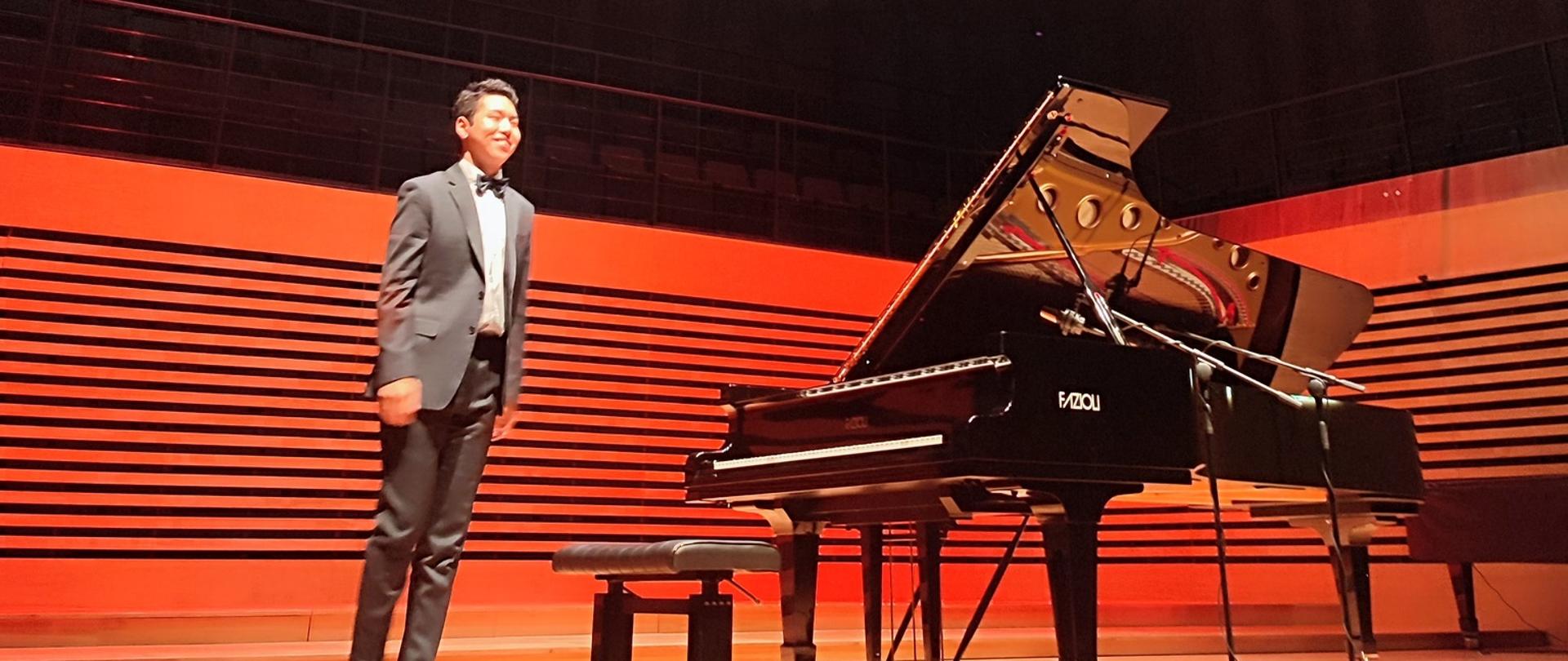 Uśmiechnięty mężczyzna stoi przy fortepianie Fazioli