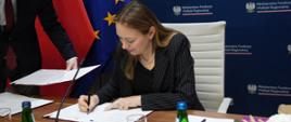 Minister funduszy i polityki regionalnej Katarzyna Pełczyńska-Nałęcz podczas podpisywania umowy na wsparcie inkubatorów na innowacje społeczne, minister siedzi przy stole i podpisuje dokument