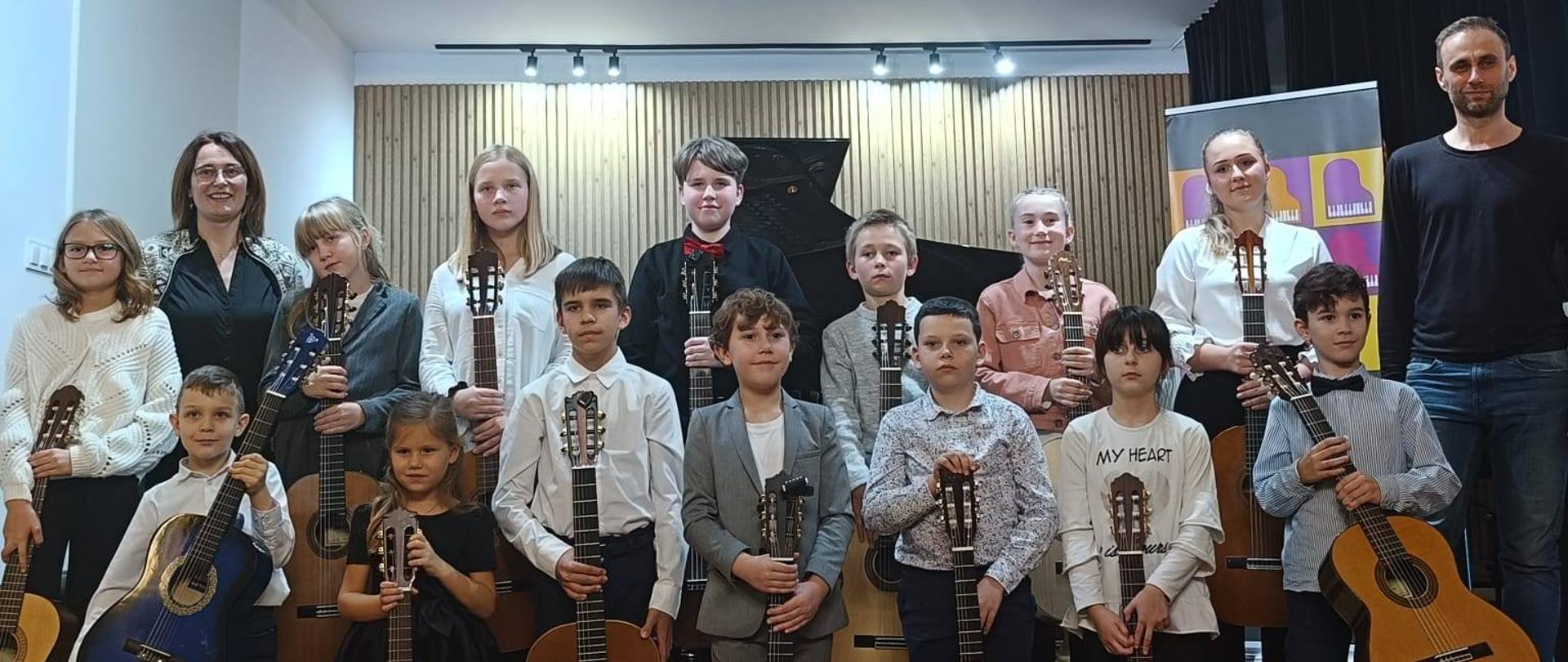 Galeria 19 zdjęć z koncertu uczniów klasy gitary A. Kozakowskiej i D. Masa, który odbył się 04 listopada 2025 w sali koncertowej w PSM w Kłodzku, uczniowie grają na gitarze na scenie.