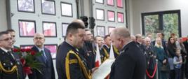 Komendanci Wojewódzki i Miejski stoją na środku przed nimi prezes OSP i gratulują mu nowego samochodu. Za nimi inni strażacy i policjanci w mundurach i zaproszeni goście po cywilnemu. 