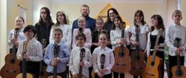 Grupowe zdjęcie uczniów uczestniczących w koncercie uczniów z klasy gitary A. Kozakowskiej i W. Kozakowskiego - 17 marca 2023, uczniowie stoją i trzymają gitary. Zdjęcie wykonane w auli PSM I st. w Kłodzku