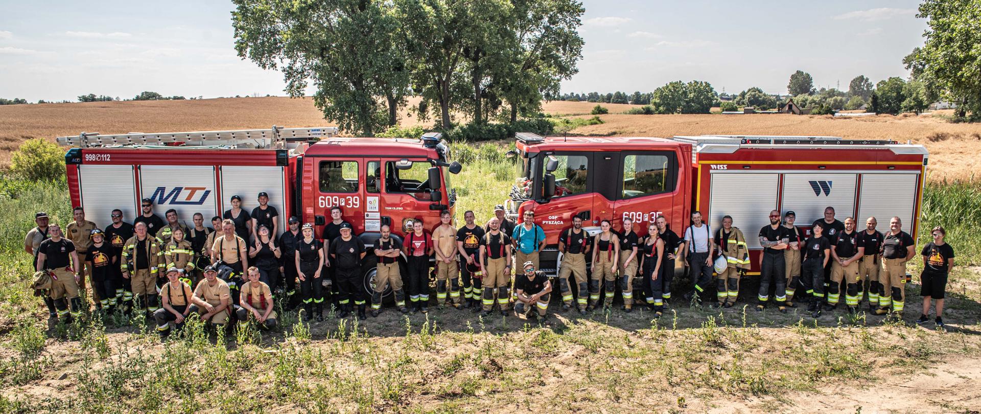 Zdjęcie zbiorowe strażaków biorących udział w szkoleniu a tle samochodów strażackich