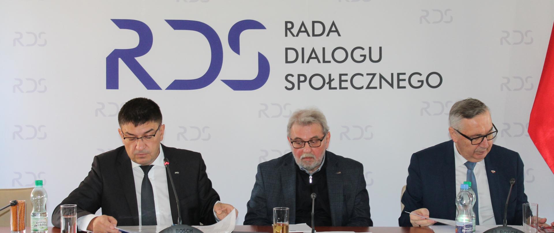 Zdjęcie przedstawia stół prezydialny, za którym siedzą: Wojciech Ilnicki, Przewodniczący Zespołu ds. rozwoju dialogu społecznego, Pan Henryk Nakonieczny, Przewodniczący Zespołu ds. prawa pracy oraz Pan Stanisław Szwed, Sekretarz Stanu w Ministerstwie Rodziny i Polityki Społecznej. W tle znajduje się baner z napisem Rada Dialogu Społecznego.