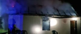 Widać budynek gospodarczy, spalony dach, z konstrukcji dachu wydobywa się dym jest noc