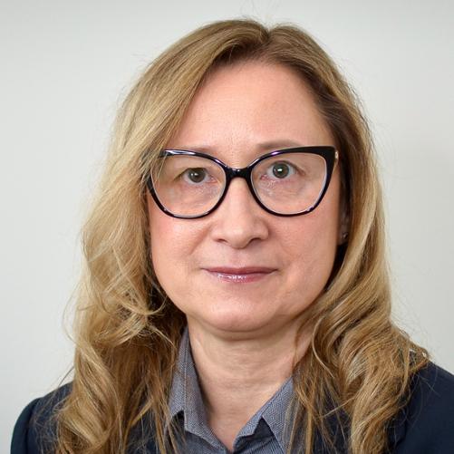 Kobieta w ciemnej marynarce, jaśniejszej bluzce, okularach, z jasnymi, długimi włosami.