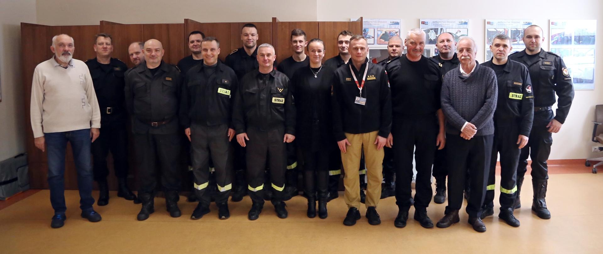 Grupowe zdjęcie strażaków CS PSP, którym wręczony został patent żeglarski (13 osób) w towarzystwie Zastępcy Komendanta Centralnej Szkoły PSP oraz przedstawicieli Regionalnego Wodnego Ochotniczego Pogotowia Ratunkowego (trzech mężczyzn oraz kobieta)