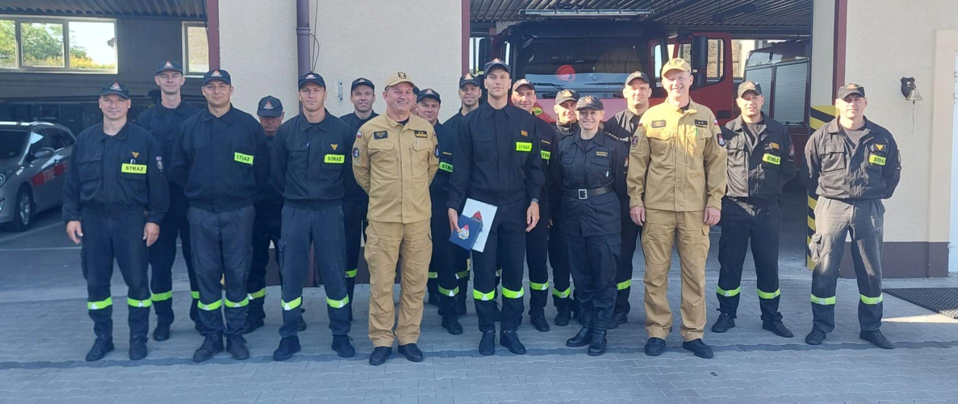 Zsjęcie przedstawia grupowę zdjęcie strażaków na tle bramy garażowej.