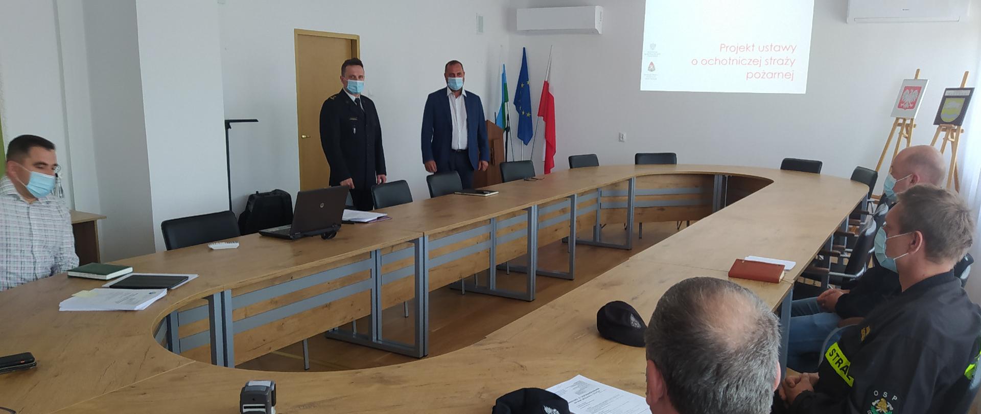 Widoczna sala z dużym stołem, duży ekran z wyświetlona treścią, na sali przedstawiciel Komendy PSP w Hajnówce oraz przedstawiciele osp z terenu powiatu hajnowskiego