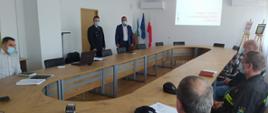 Widoczna sala z dużym stołem, duży ekran z wyświetlona treścią, na sali przedstawiciel Komendy PSP w Hajnówce oraz przedstawiciele osp z terenu powiatu hajnowskiego