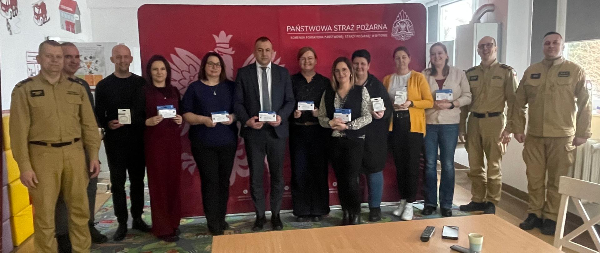 Uczestnicy spotkania pozują do zdjęcia na tle czerwonego baneru Państwowa Straż Pożarna. 