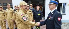 Zdjęcie przedstawia st. bryg. Andrzeja Góreckiego Komendanta Powiatowego PSP w Brodnicy wręczającego asp. sztab. Robertowi Maciejewskiemu decyzję o przyznaniu nagrody z okazji jubileuszu 30 lat służby w szeregach Państwowej Straży Pożarnej. W tle strażacy podziału bojowego JRG w Brodnicy.