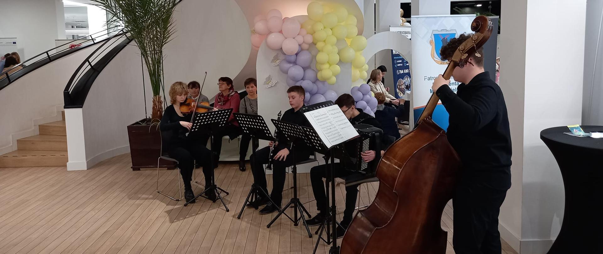 zespół kameralny prowadzony przez Zdzisława Szymczyka w składzie skrzypce, klarnet, akordeon i kontranbas podczas koncertu z okazji Dnia Kobiet na holu Miejskiej Biblioteki Publicznej