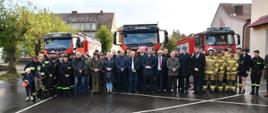 Zdjęcie grupowe uczestników ceremonii przekazania samochodu. W tle park maszynowy OSP Ińsko.