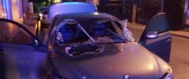 Zdjęcie przedstawia szary samochód osobowy BMW ze spalona maską przednią. 