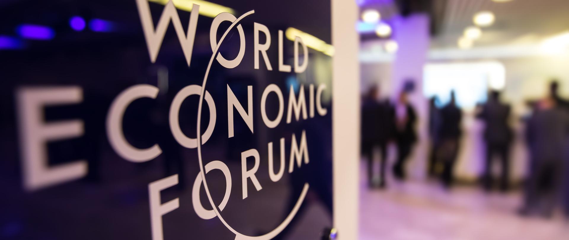 Napis World Econimic Forum a w tle rozmyte postacie