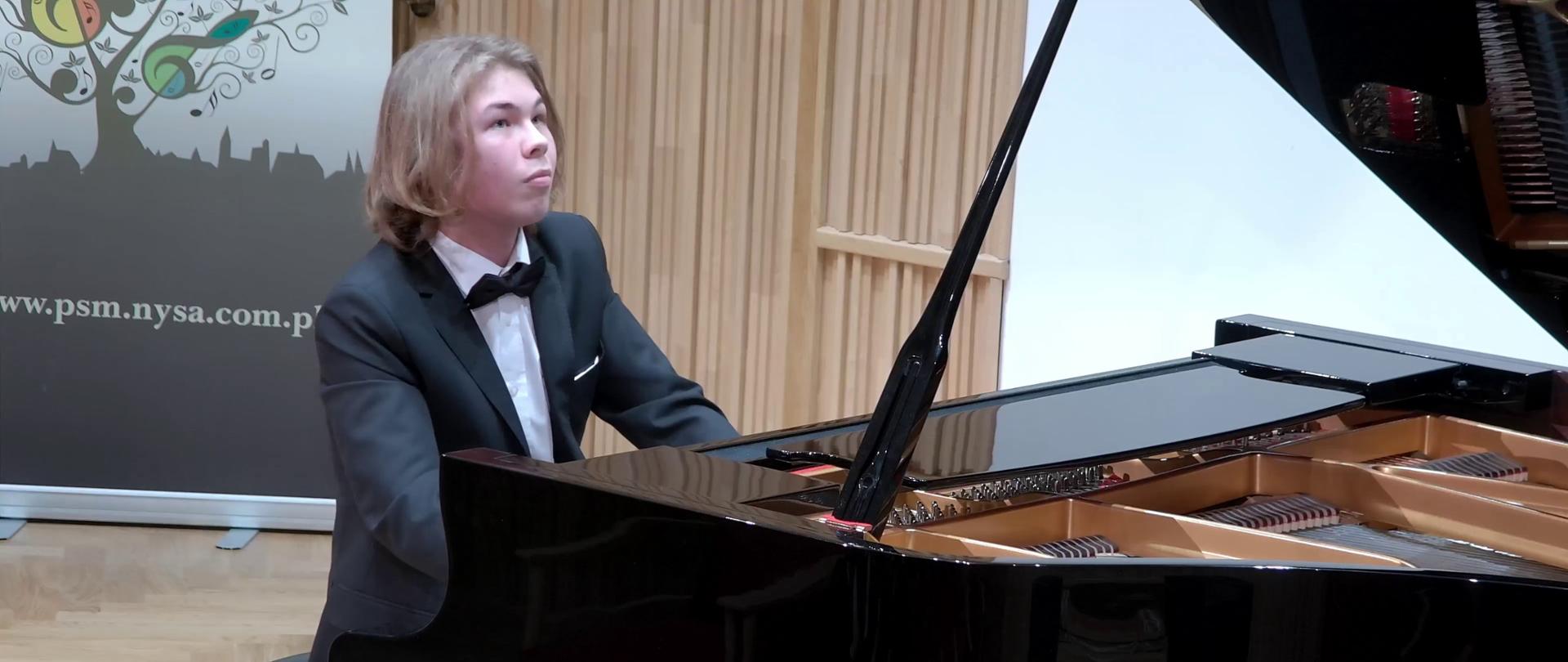 Zdjęcie. Na estradzie Sali Koncertowej PSM I i II stopnia w Nysie na czarnym fortepianie gra młody pianista - Wojciech Walasek.