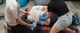 Dwoje osoby zakładają poszkodowanemu opatrunek w okolicach nerek. Obok jest apteczka ppp.