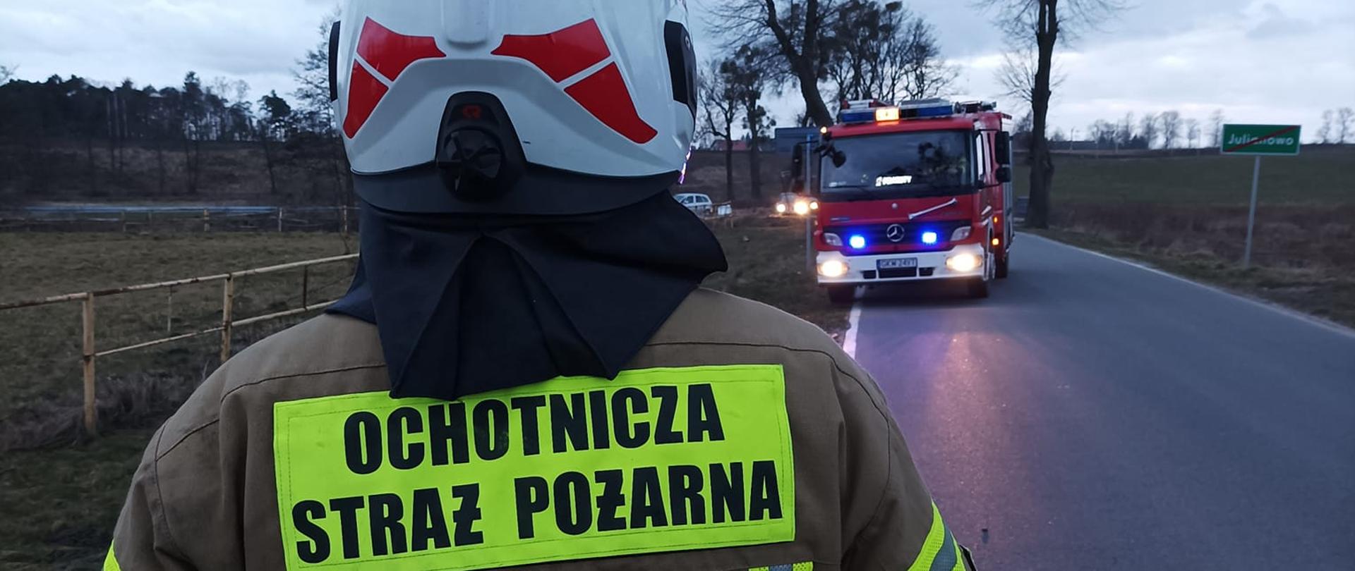 Strażak OSP Prabuty stoi na jezdni w tle pojazd ratowniczy