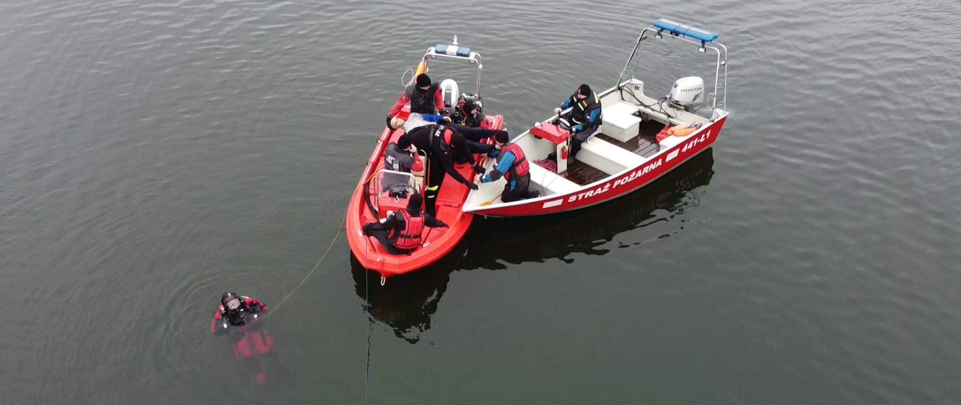 Obraz przedstawia strażaków na dwóch łodziach ratowniczych. Obok nurek.