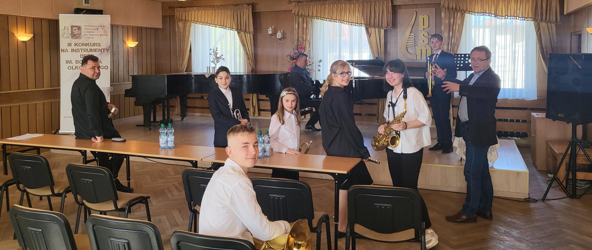 Fotografia przedstawiająca nauczycieli i uczniów z instrumentami w sali koncertowej