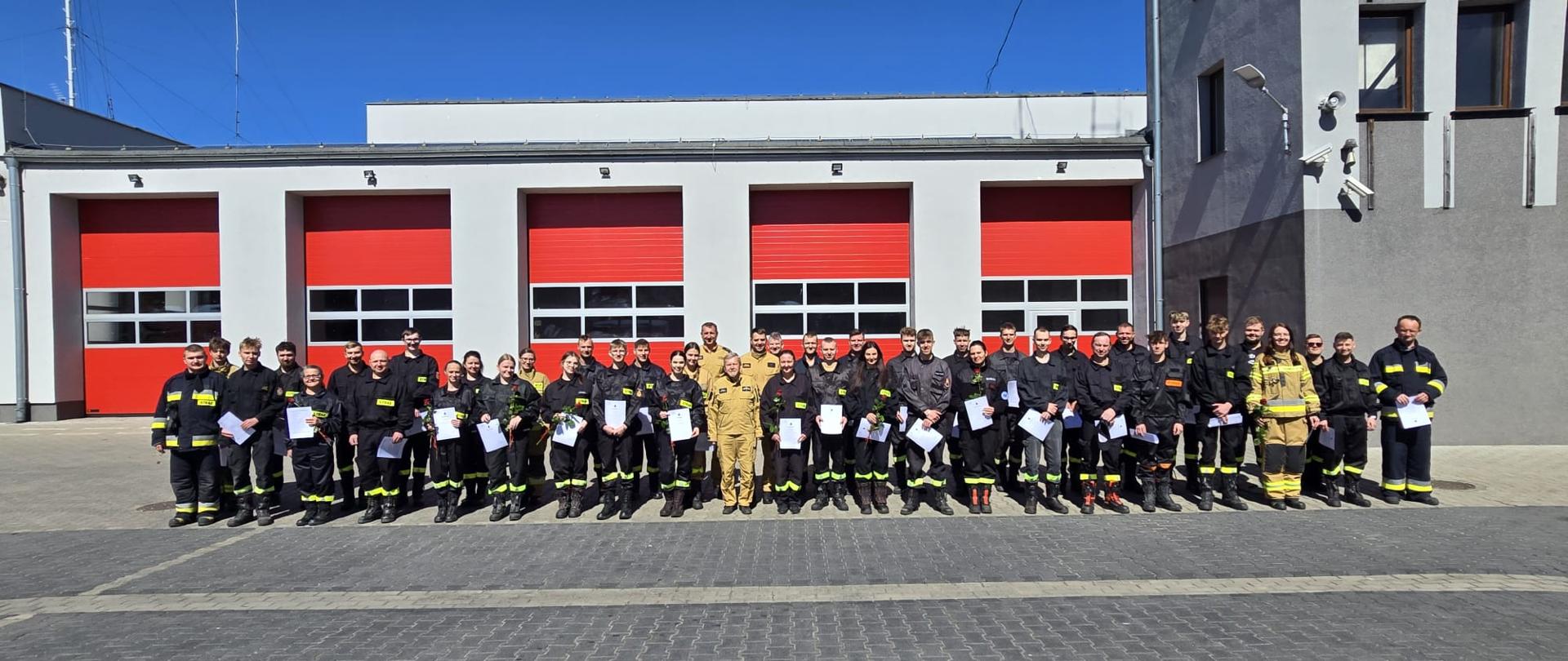 Strażacy na zdjęciu grupowym na tle komendy powiatowej