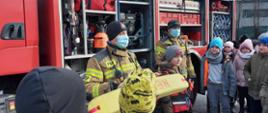 Na zdjęciu strażacy pokazują samochód ratowniczy i sprzęt dzieciom ze szkoły