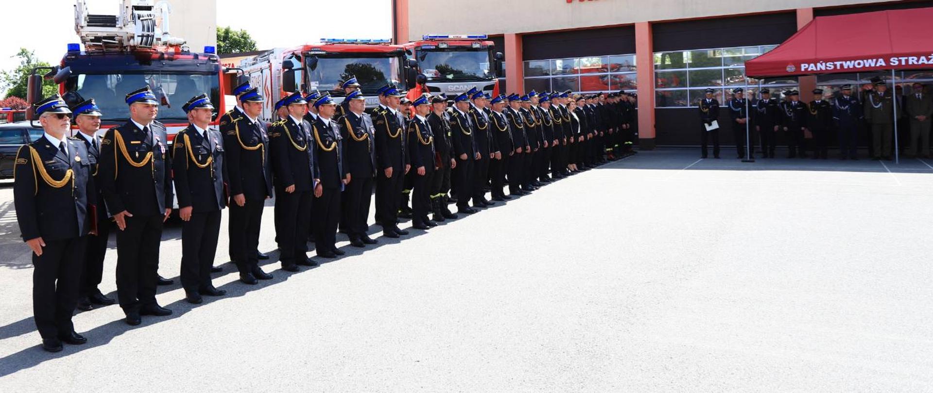 Strażacy KP PSP Oleśnica stoją w dwuszeregu w umundurowaniu wyjściowym. 