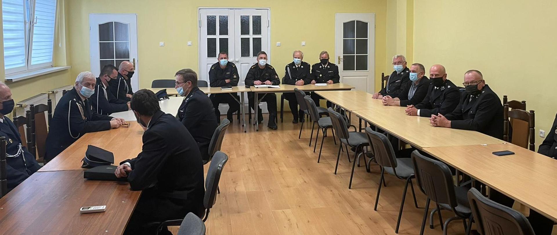 Widać strażaków siedzących przy stołach podczas spotkania