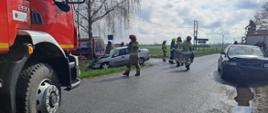 Zdjęcie przedstawia wóz strażacki, karetkę pogotowia ratunkowego oraz dwa pojazdy po kolizji drogowej. Strażaków PSP i OSP podczas działań ratowniczych.