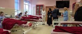 Minister Wieczorek i kilka osób stoi w sali, w której nad szpitalnymi łózkami pochylają się studenci.