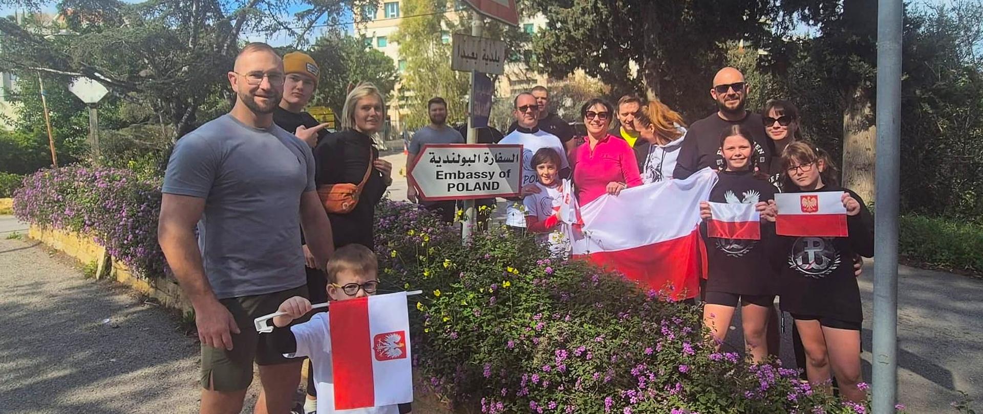 A group of people in sportswear stand on the street with Polish flags.