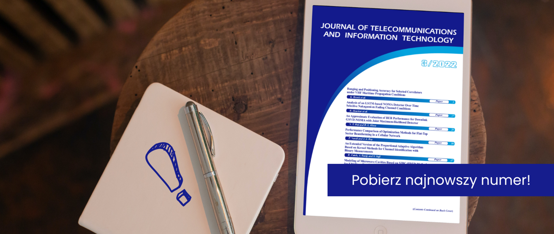 Na ilustracji zdjęcie okrągłego stolika, na którym leży tablet z wyświetloną pierwszą stroną okładki kwartalnika oraz długopis z notatnikiem. Ma pierwszym planie napis: Pobierz najnowszy numer!