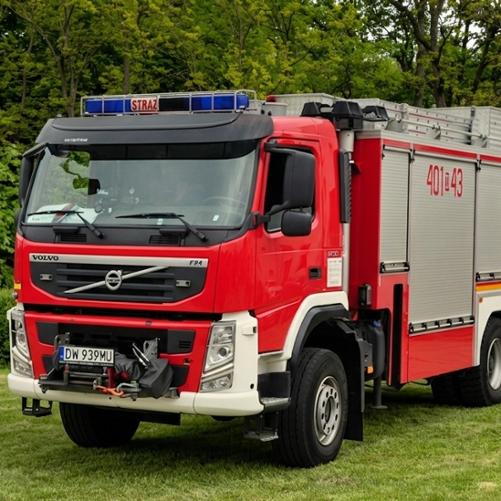 Ciężki samochód ratownictwa technicznego Volvo FM. Czerwone nadwozie z numerem na szarej skrytce „401[D]43”. Pojazd stoi na zielonej trawie w tle widać las liściasty.