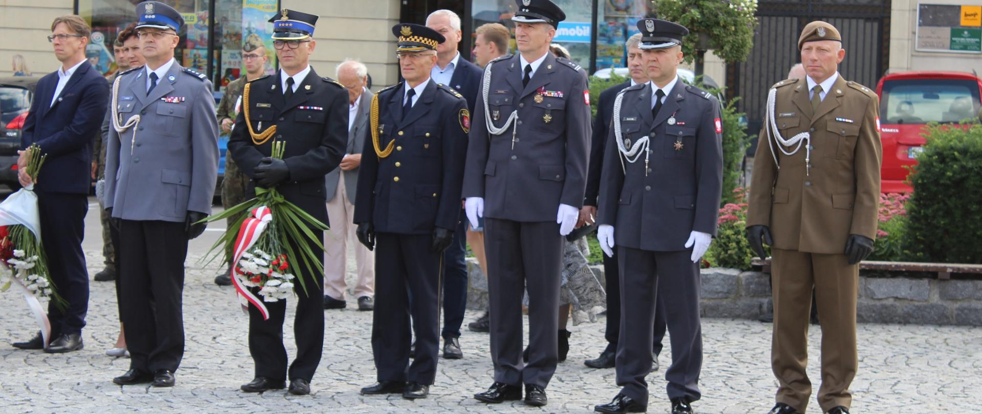NA zdjęciu przedstawiciele służb mundurowych podczas uroczystsi za nimi klomb zieleni 