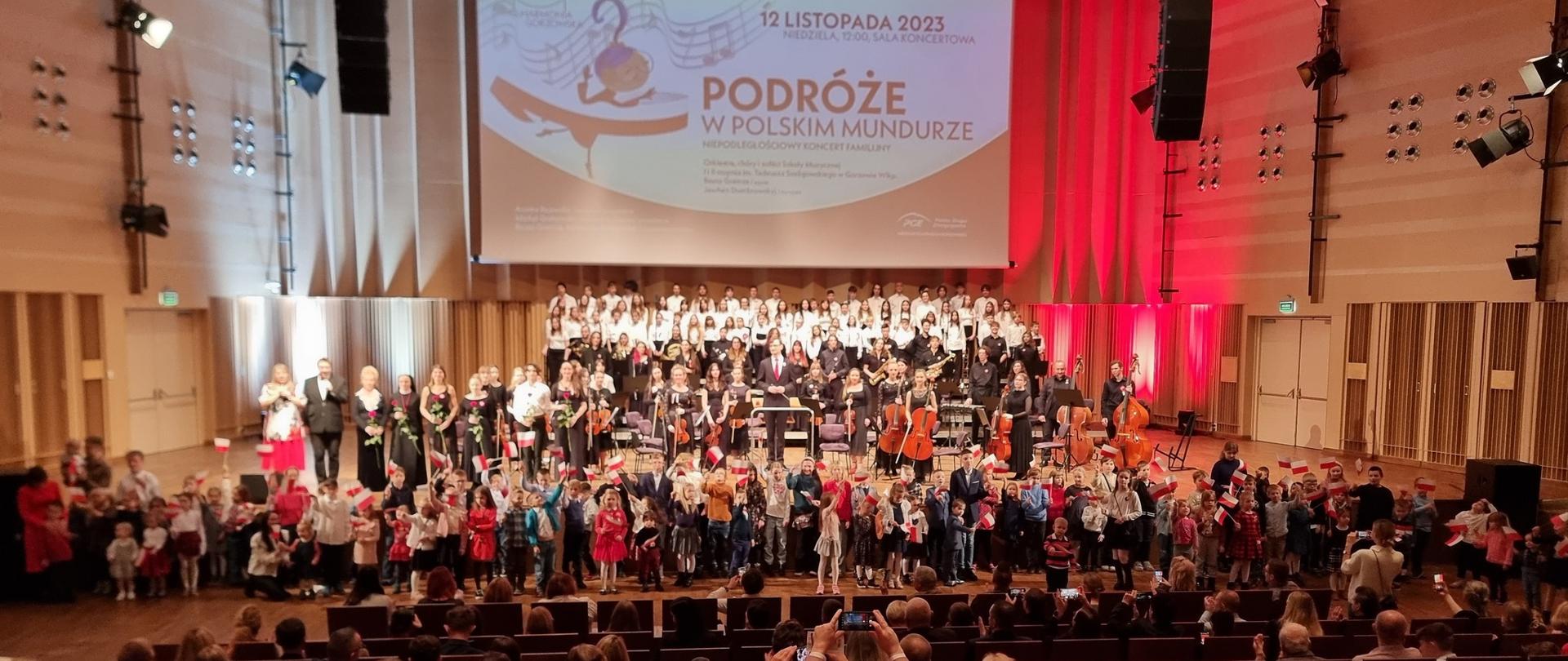 Zbiorowe zdjęcie z koncertu patriotycznego - wykonawcy i dzieci z biało-czerwonymi chorągiewkami