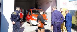 Pięć osób ogląda garaż i samochód pożarniczy. Trzy osoby są w mundurach