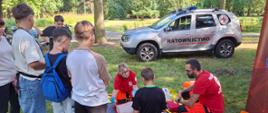 Na zdjęciu widoczni są ratownicy z Polskiego czerwonego krzyża podczas pokazywania jak pomóc osobie poszkodowanej. Wokół nich jest młodzież słuchająca wykładu.