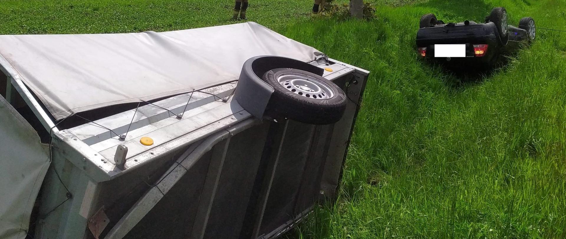 Samochód osobowy znajduję się na dachu w rowie, za nim leży przewrócona przyczepka