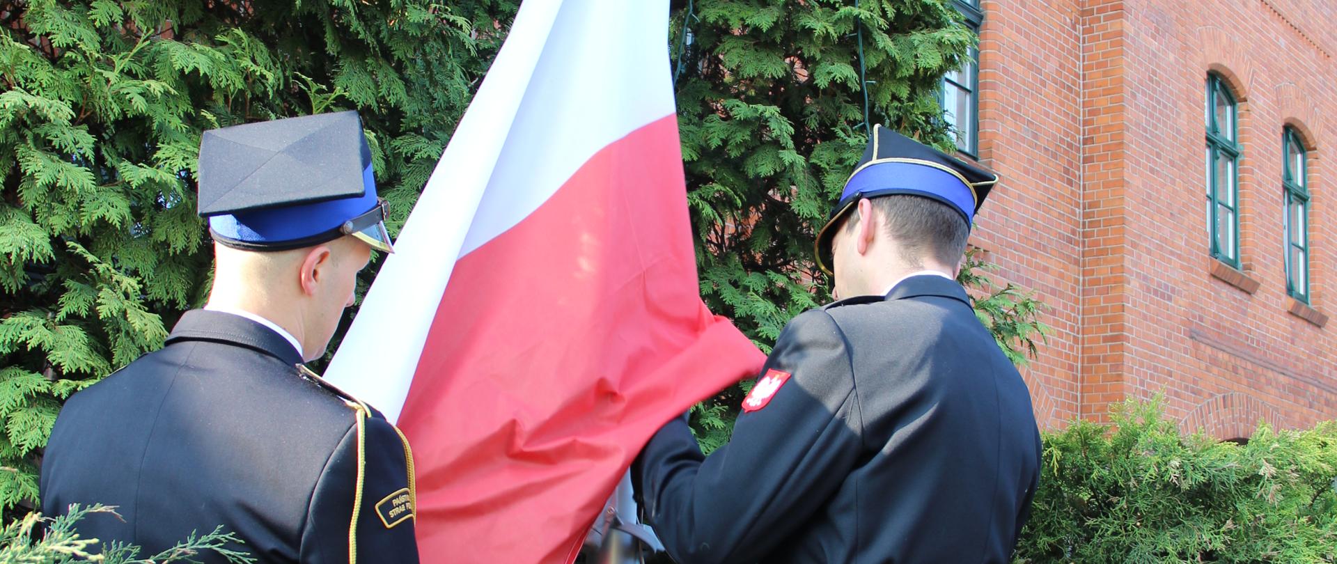 Poczet flagowy komendy uroczyscie przypina flagę do masztu. W tle budynek komendy.