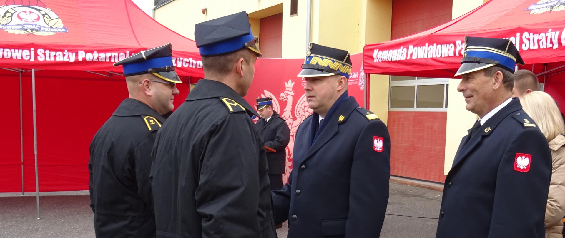 czterech strażaków w rogatywkach , za nimi czerwony namikot oraz bramy garażowe