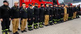 Szyk wyznaczonych ratowników przed szeregiem czerwonych samochodów pożarniczych; formowanie pododdziału do ćwiczeń.