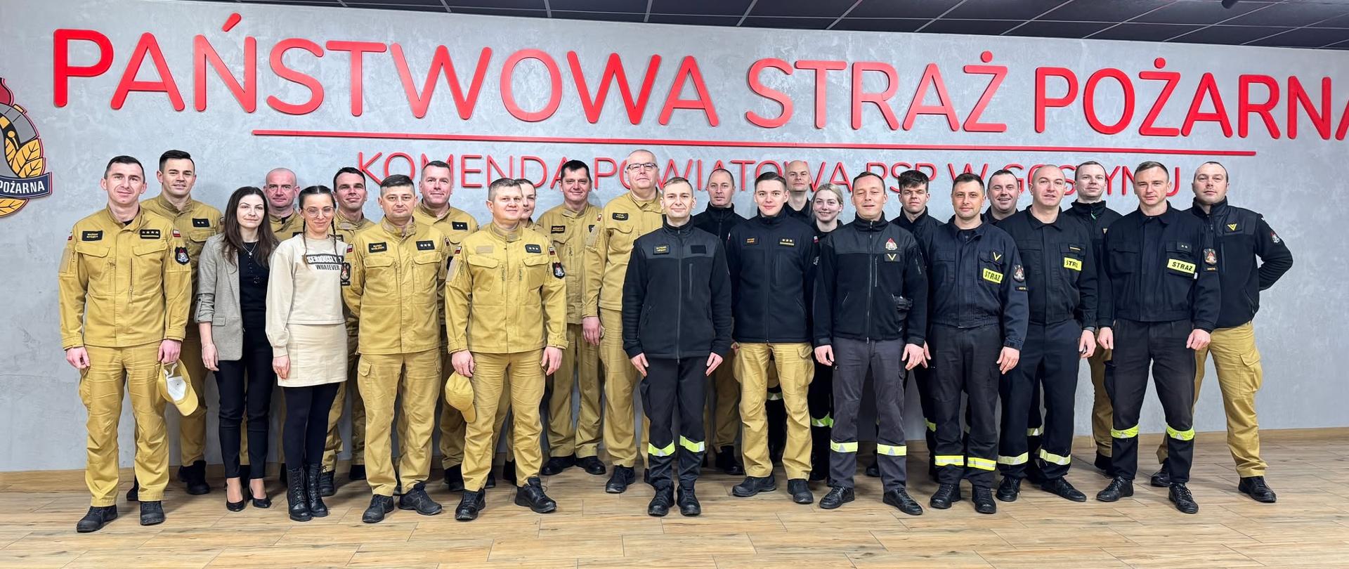 Grupowe zdjęcie strażaków na tle napisu.