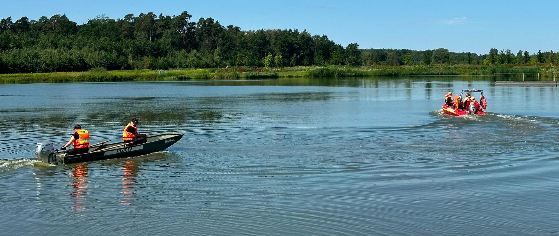 Na zalewie płyną strażacy łódkami, w tle drzewa