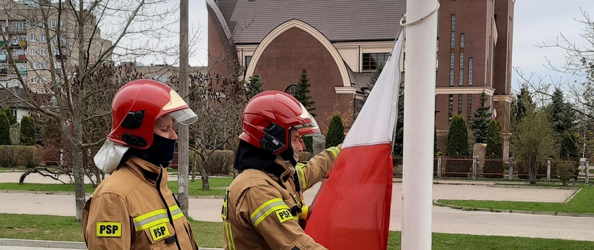 Zdjęcie przedstawia 3 strażaków zawieszających flagę na maszt