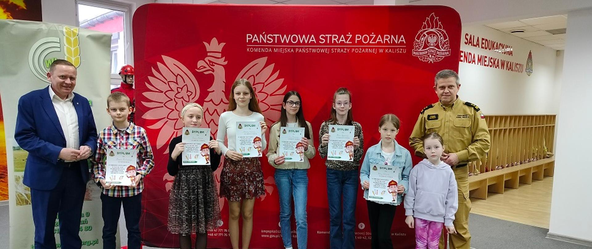 Komendant pozuje do zdjęcia razem z dziećmi na tle banera PSP.